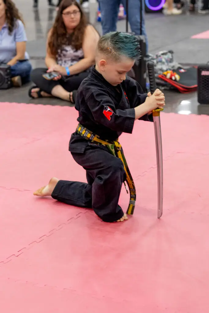 young boy kneeling with a martial arts sword